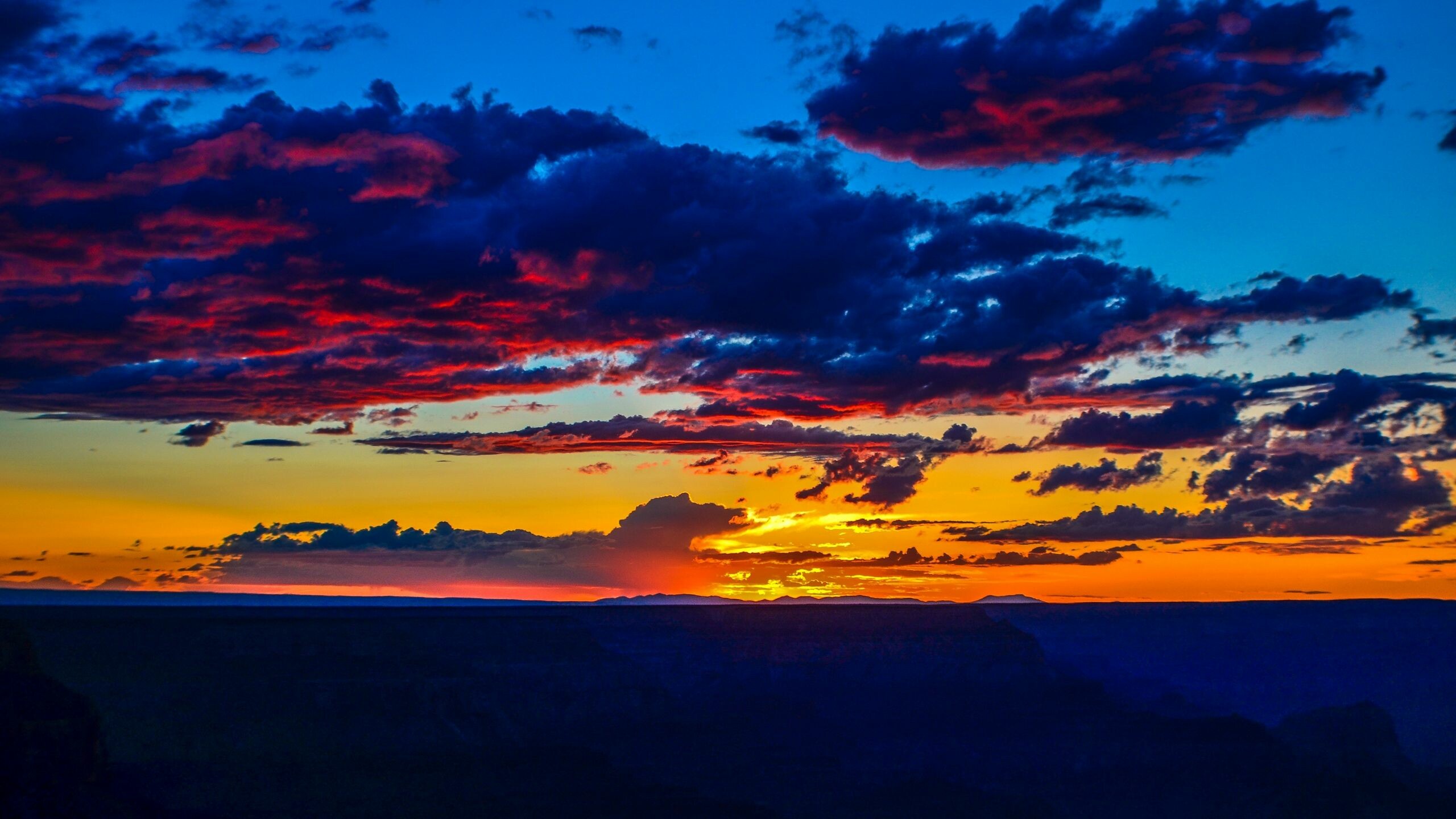 Layered canyon ridge silhouette, Vivid red cloud sky, Orange horizon afterglow Layered canyon ridge silhouette, Vivid red cloud sky, Orange horizon afterglow — 2560×1440 HD wallpaper