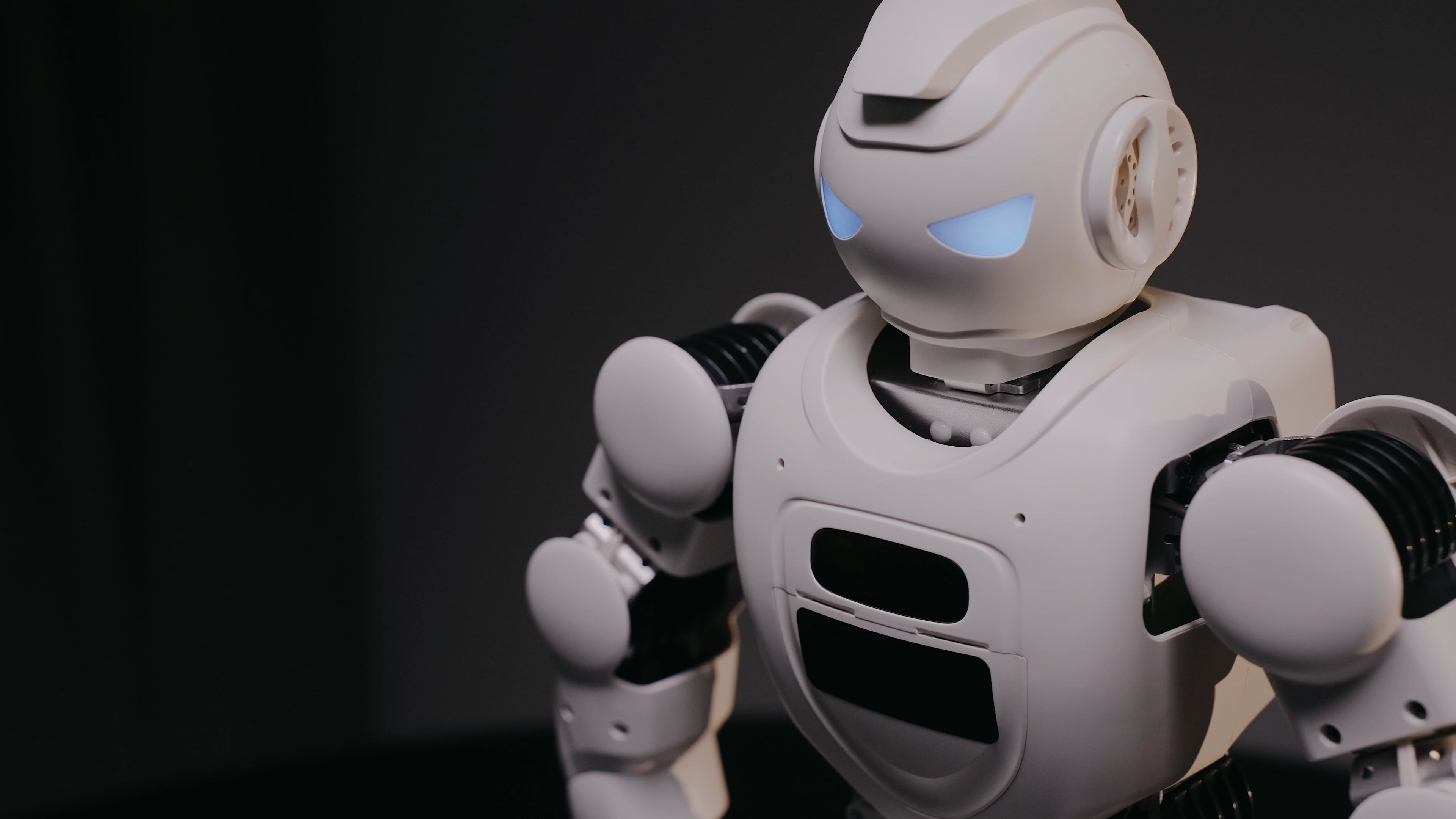 White humanoid robot, Glowing blue LED eyes, Dark studio backdrop White humanoid robot, Glowing blue LED eyes, Dark studio backdrop — 3840×2160 HD wallpaper