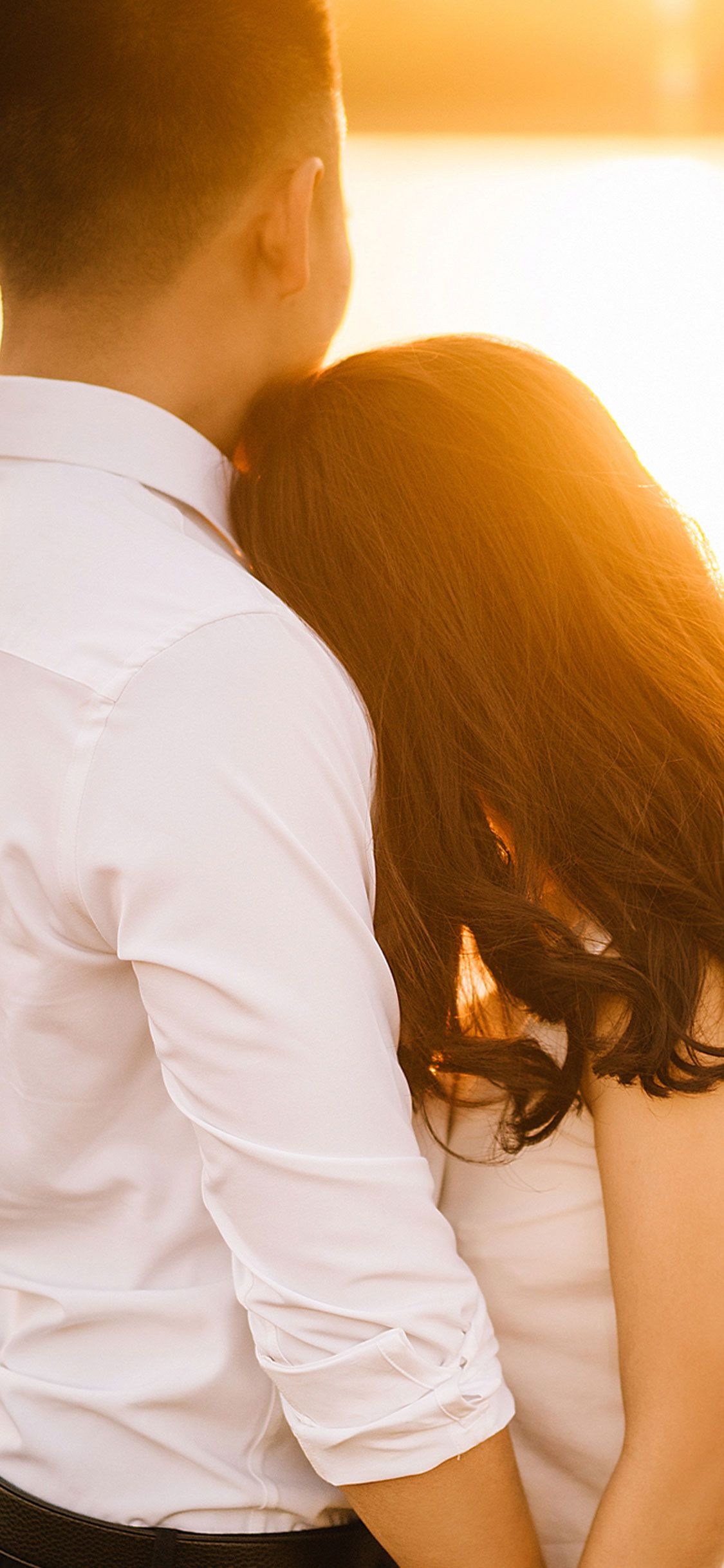 Couple embracing back view, Woman resting on shoulder, Warm golden sunset backlight Couple embracing back view, Woman resting on shoulder, Warm golden sunset backlight — 1125×2436 HD wallpaper